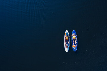 Concept Summer active sport on water. Funny man and woman floats on supboard on lake, top view from drone
