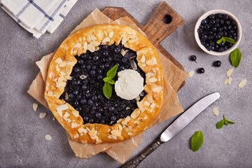 Galette with blueberries, almond petals and vanilla ice cream scoop. Delicious homemade open sweet pie tart with seasonal berries.