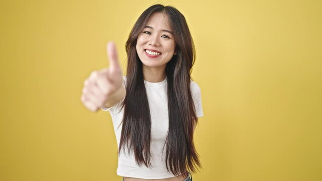 Young chinese woman smiling confident doing ok sign with thumb up over isolated yellow background