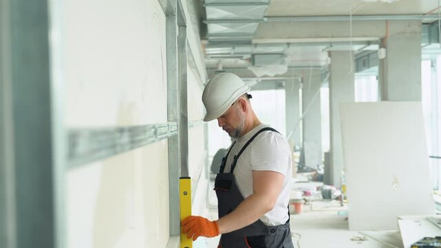 A man builder measures of the vertical deviation of plasterboard wall. Bubble level ruler