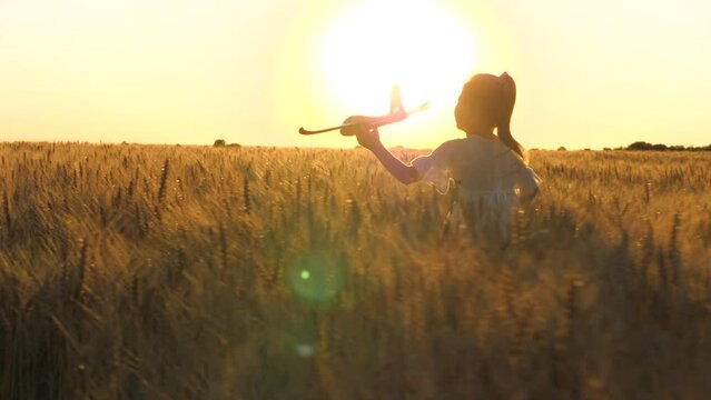 little child girl daughter runs through wheat field with toy plane her hand sunset. happy family dream fly. sunset field, happy runs through wheat field, child launches plane, child dreams flying sky