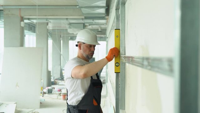 A man builder measures of the vertical deviation of plasterboard wall. Bubble level ruler