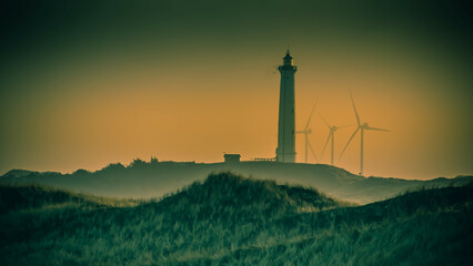 Fototapeta na wymiar Ein Leuchtturm und eine Gruppe von Windkrafträder bei Sonnenuntergang an der dänischen Nordseeküste