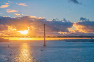 View of 25 de Abril Bridge famous tourist landmark of Lisbon connects Lisboa and Almada on Setubal Peninsula over Tagus river with tourist yacht silhouette at sunset and flying plane. Lisbon, Portugal