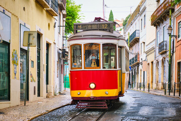 Naklejka na ściany i meble Famous vintage yellow tram in the narrow streets of Alfama district in Lisbon, Portugal - symbol of Lisbon, famous popular travel destination and tourist attraction