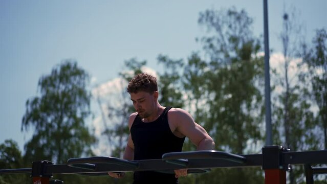 portrait of a young sportsman working out on parallel bars swinging his arms and shoulders doing push-ups on sports ground during street training