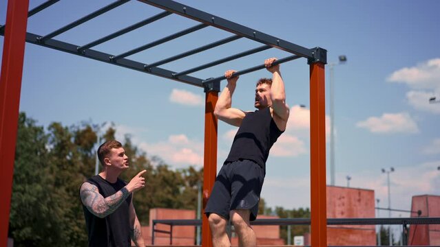 Personal fitness trainer or bodybuilder trains young athlete working out on sports ground motivation support