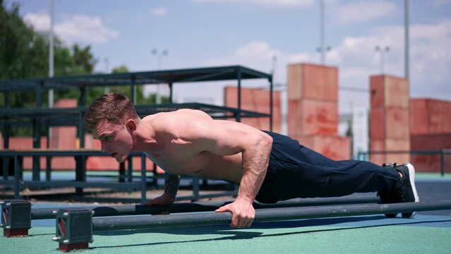 young pumped-up athlete doing push-ups from the ground during street training endurance exercise swings arms and shoulders