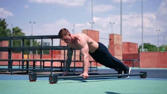 young pumped-up athlete doing push-ups from the ground during street training endurance exercise swings arms and shoulders