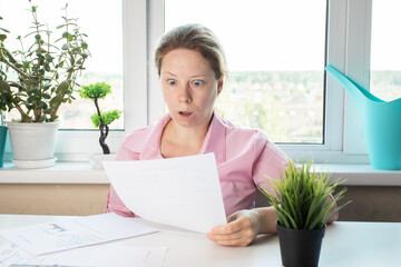 woman surprised by utility bills, Shocked woman looking at letter, reviewing papers with bank...
