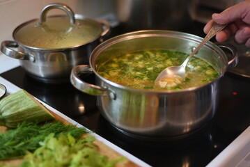 There is a metal saucepan with cooking soup on the electric stove. The soup was scooped up with a spoon to determine its readiness.