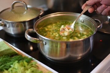 There is a metal saucepan with cooking soup on the electric stove. The soup was scooped up with a spoon to determine its readiness.