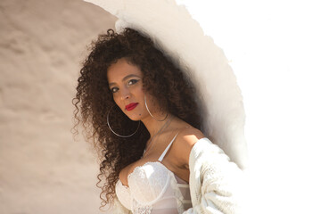 A middle-aged Spanish woman with dark, curly hair, dressed in jeans and a white lace top, is...