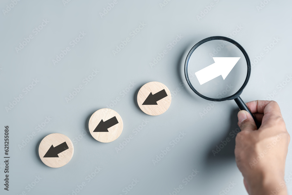 Aufkleber Hand holding magnifier focus to White arrow and different direction facing opposite direction with black arrow for business disruption and technology transformation and different thinking idea
