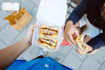 POV top down photo of woman hold delicious sandwich in take away box. Street food festival or food truck concept. Fast food with organic ingridients. Sharing concept