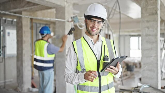 Two men builders smiling confident using touchpad at construction site