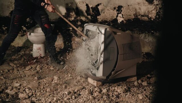 The guy smashes the screen of an old TV with a sledgehammer. Fragments from the screen fly apart. Slow motion shots