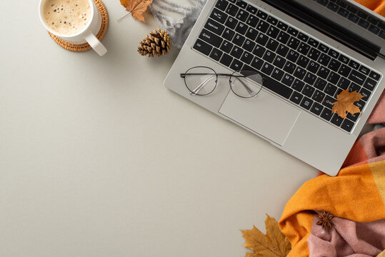 Top view image encapsulates the essence of working from home, showcasing a laptop with a cozy blanket, pinecones, spices, glasses and a cup of coffee on grey isolated backdrop with copyspace for text