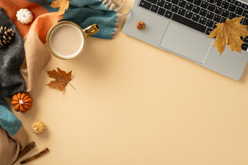 Fall-themed workspace arrangement. Top view of laptop, mug of steaming coffee, cozy plaid, petite pumpkins, golden leaves, pine cone, cinnamon on pastel beige surface, with empty area for text or ad