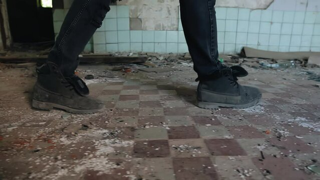 The legs of a man walking through an abandoned room on garbage and junk. Taking a close-up of the legs