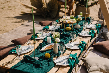 Lunch, romantic green colors. Picnic with blanket, napkin, pillows, candles, wooden decor, dry flowers. Bachelorette party on beach. Boho style design picnic. Decorations for celebration birthday.