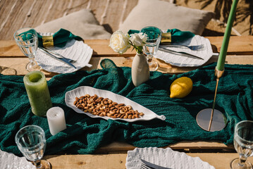 Picnic with wooden decor, candles, flowers. Bachelorette party on beach. Boho style design picnic. Decorations for celebration birthday. Wedding outdoors. Summer picnic with blanket, napkin, pillows.