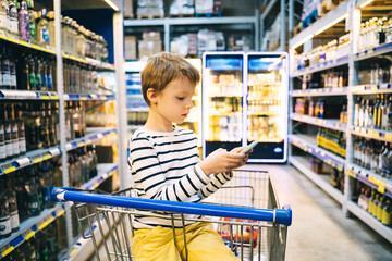 Preschool boy sits in shopping cart in alcohol department.