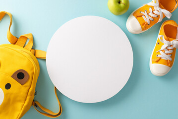 Make your educational message stand out with a top view photo of yellow child backpack complemented by a pair of sneakers and apple on a light blue background with empty circle for text or advert