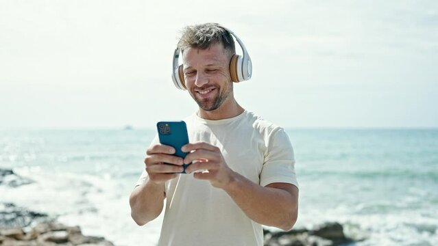 Young man using smartphone wearing headphones at the beach