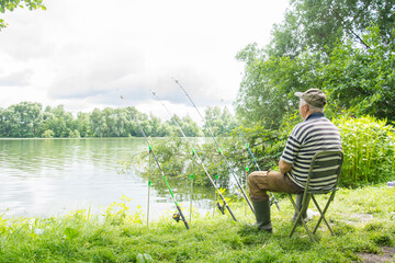 In summer, a man sits near the river and catches fish.