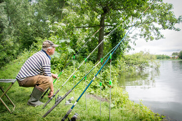 In summer, a man sits near the river and catches fish.