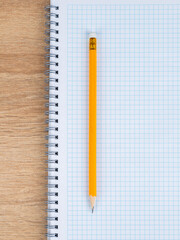 Close-up of a yellow slate pencil lying on a checkered notebook, ready to start work