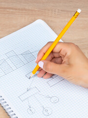 Close-up woman writes and draws a graph with a black slate pencil in a checkered notebook