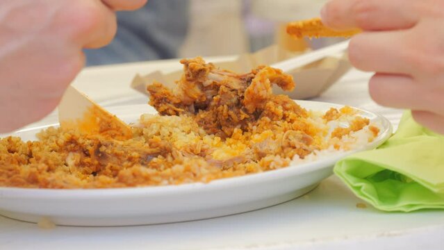 People eat a dish of rice and meat from plates with eco wooden forks and knives at a street market