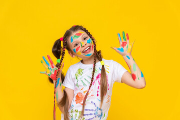 A child painted with multicolored paints. A young girl with painted palms. Creativity for schoolchildren. Drawing for children. Yellow isolated background.