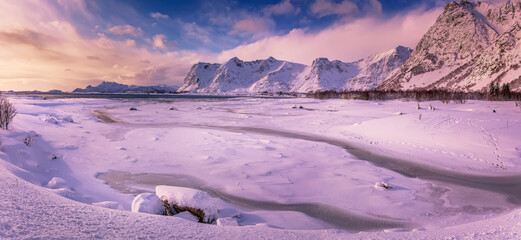 Wonderful snowy winter in Norway. Beautiful sunset with colorful dramatic sky, in amazing winter landscape of the Lofoten Islands. Snow-covered riverbed and mountains under sunlight. Creative image