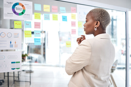 Black woman, thinking and glass board for project management, marketing or planning at office. African female person, manager or employee checking project plan, tasks or statistics at the workplace