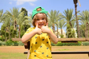 Fototapete Kanarische Inseln A cute boy invites you to the resort. The child laughs, enjoys the rest. Summer time. Tropical travel. Beautiful palm trees in the background. Copyspace