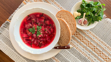 Borscht on grey tablecloth with bread and green parsley and dill