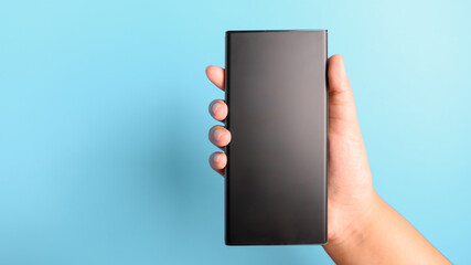 Woman hand holding black smartphone on blue background with copy space. Communication technology and Innovative gadget concept.