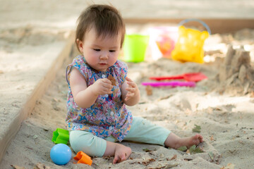 Adorable 9 months old baby playing outdoors - lifestyle portrait of mixed ethnicity Asian Caucasian baby girl playing with block toys happy and carefree at playground sitting on sand