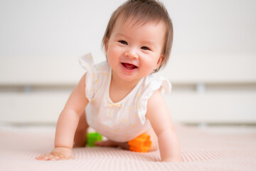 lifestyle home portrait of 9 months old mixed ethnicity Asian Caucasian baby girl playing happy and carefree on bed crawling and handling color blocks in childhood and nursery concept