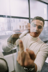 Young crazy handsome male person showing middle finger while writing on a glass wall