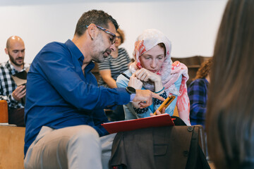 Obraz premium Middle-aged, experienced, male employee helping his muslim junior coworker. Male employee calculating on phone, he is helping his female colleague