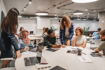 Long curly haired male employee helping his colleagues with financial charts while working with them in modern office room