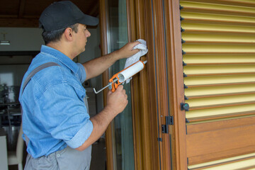 Image of a handyman who with a silicone gun closes the cracks in the window. Improve the...