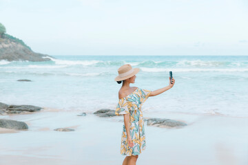 While enjoying the beach, a happy woman uses her smartphone to stay connected with the online world, effortlessly balancing tech and nature.