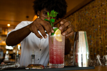 latin bartender putting a top of mint in the cocktail