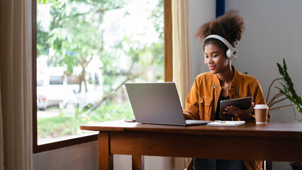 African american businesswoman working on tablet and typing business data on laptop in cafe
