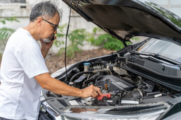Middle age man checking his broken down car's engine while on the phone with a mechanic